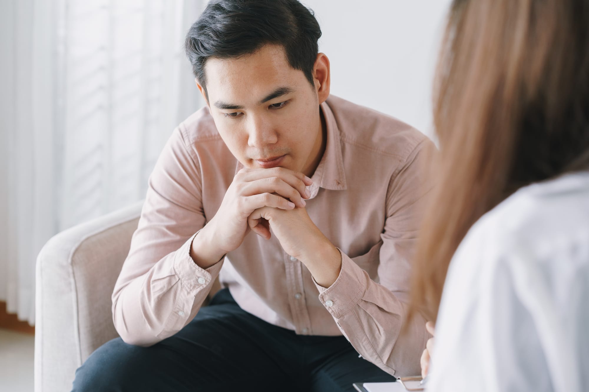 An adult man in a therapy session, listening thoughtfully with hands clasped.