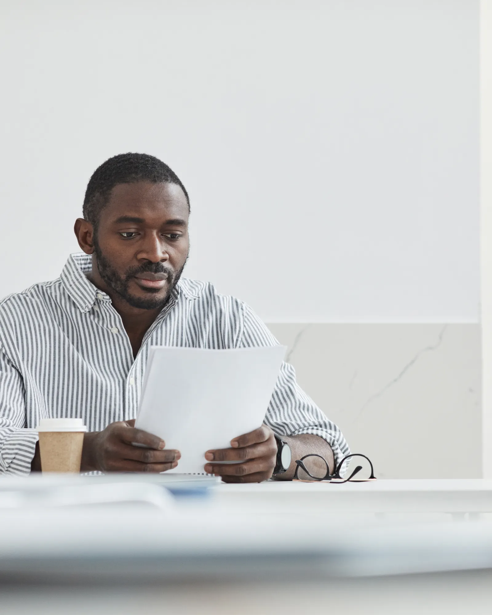 A man reading through papers with a coffee cup beside him in even, natural light.