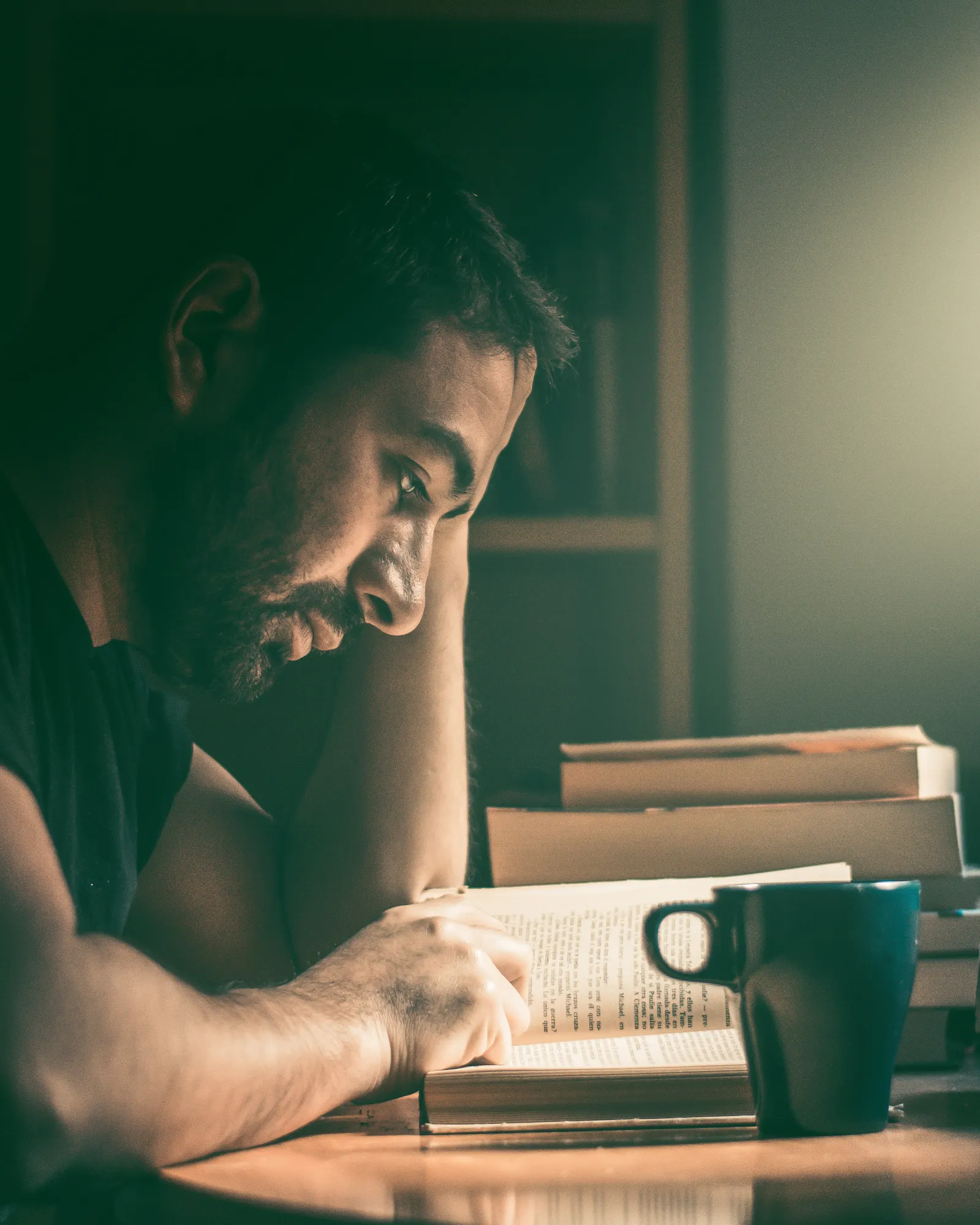 An adult man reading quietly by a window in warm daylight at home.