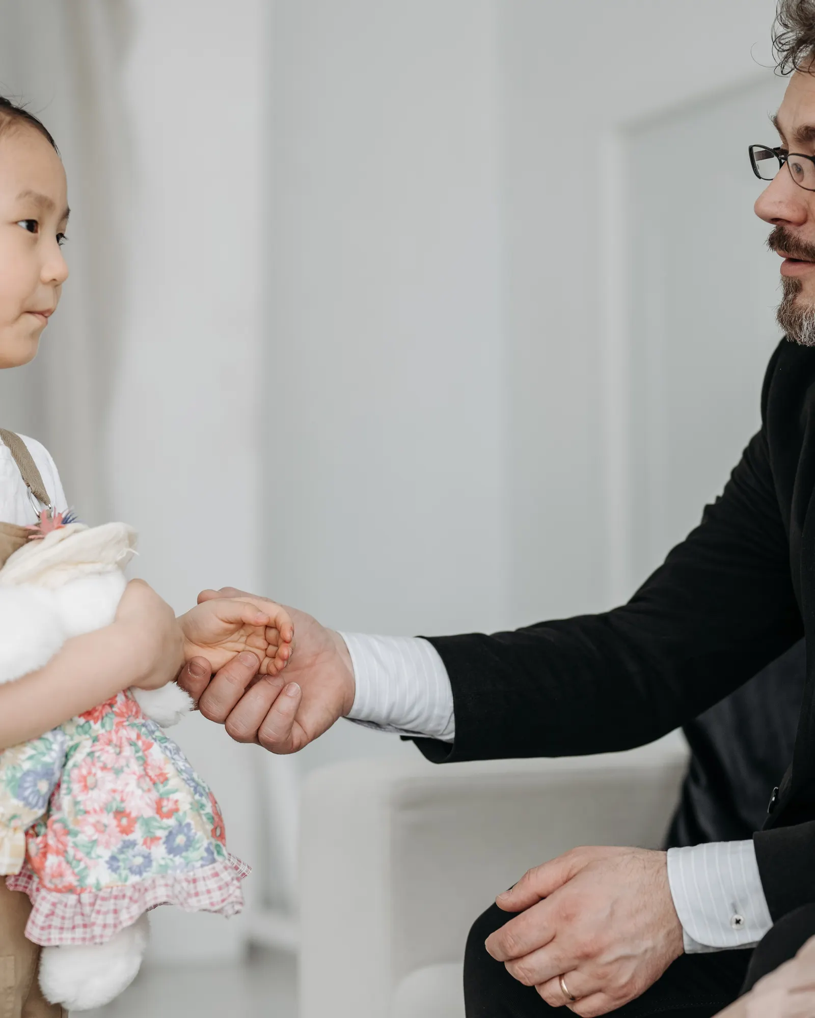 A couple meeting a young girl holding a teddy bear, all smiling, warmly lit indoors.