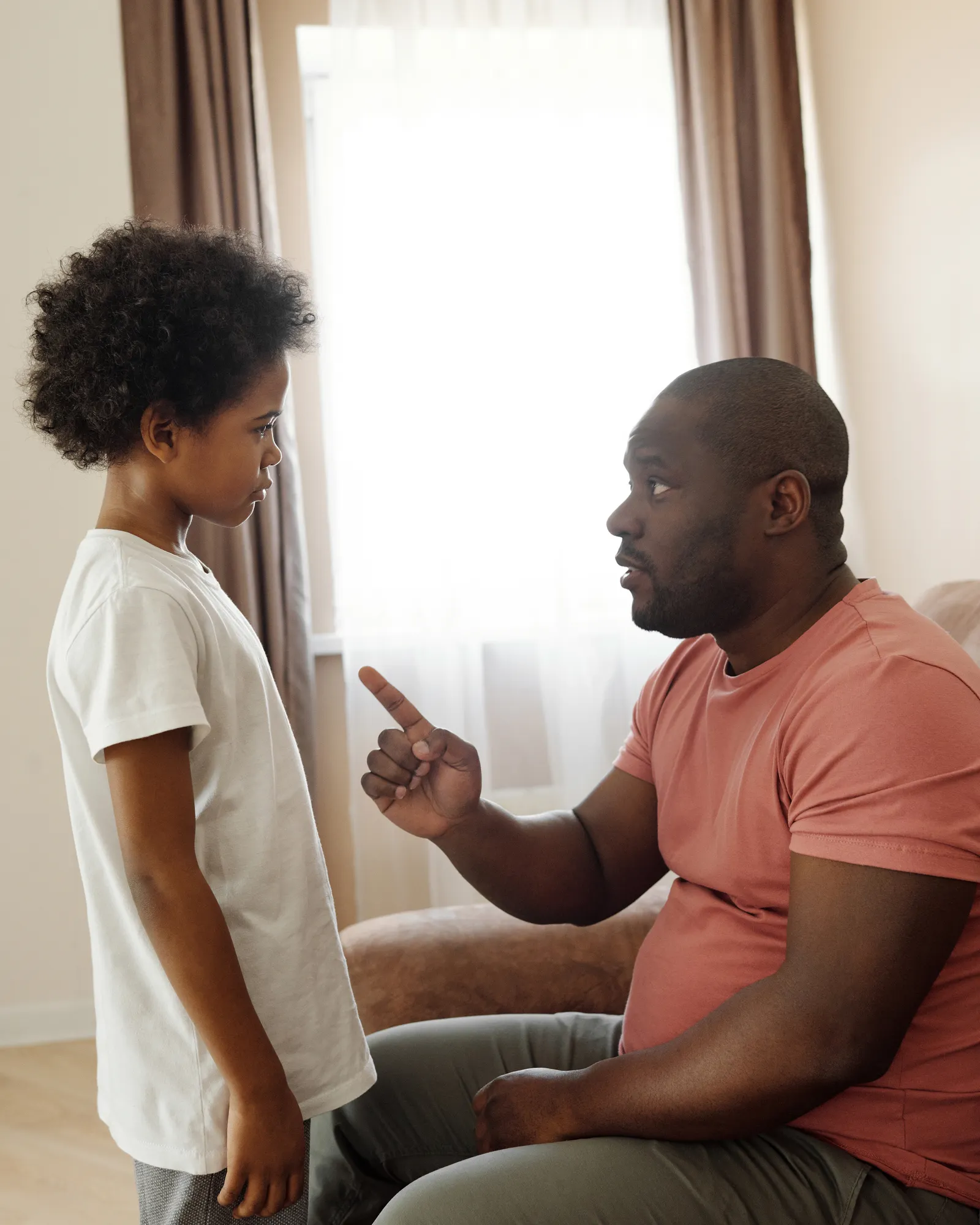 A father attentively explaining something to his young son in a cozy living room.