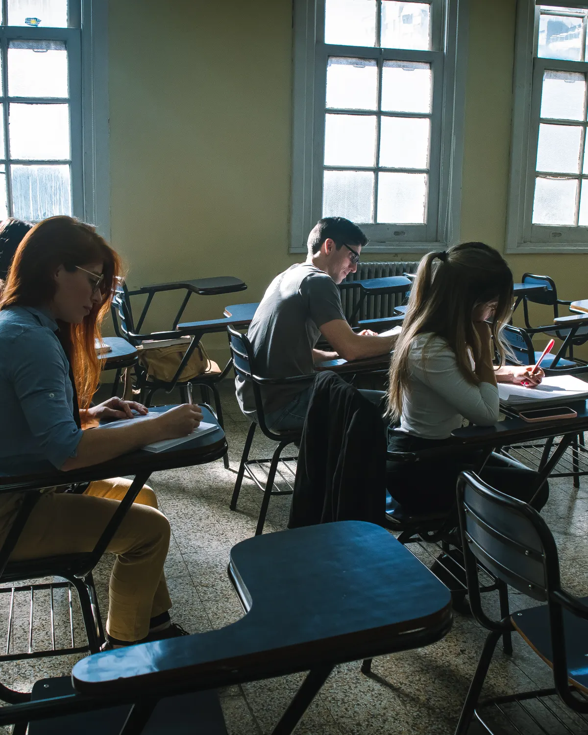 A group of students working through a test in a sunlit classroom.