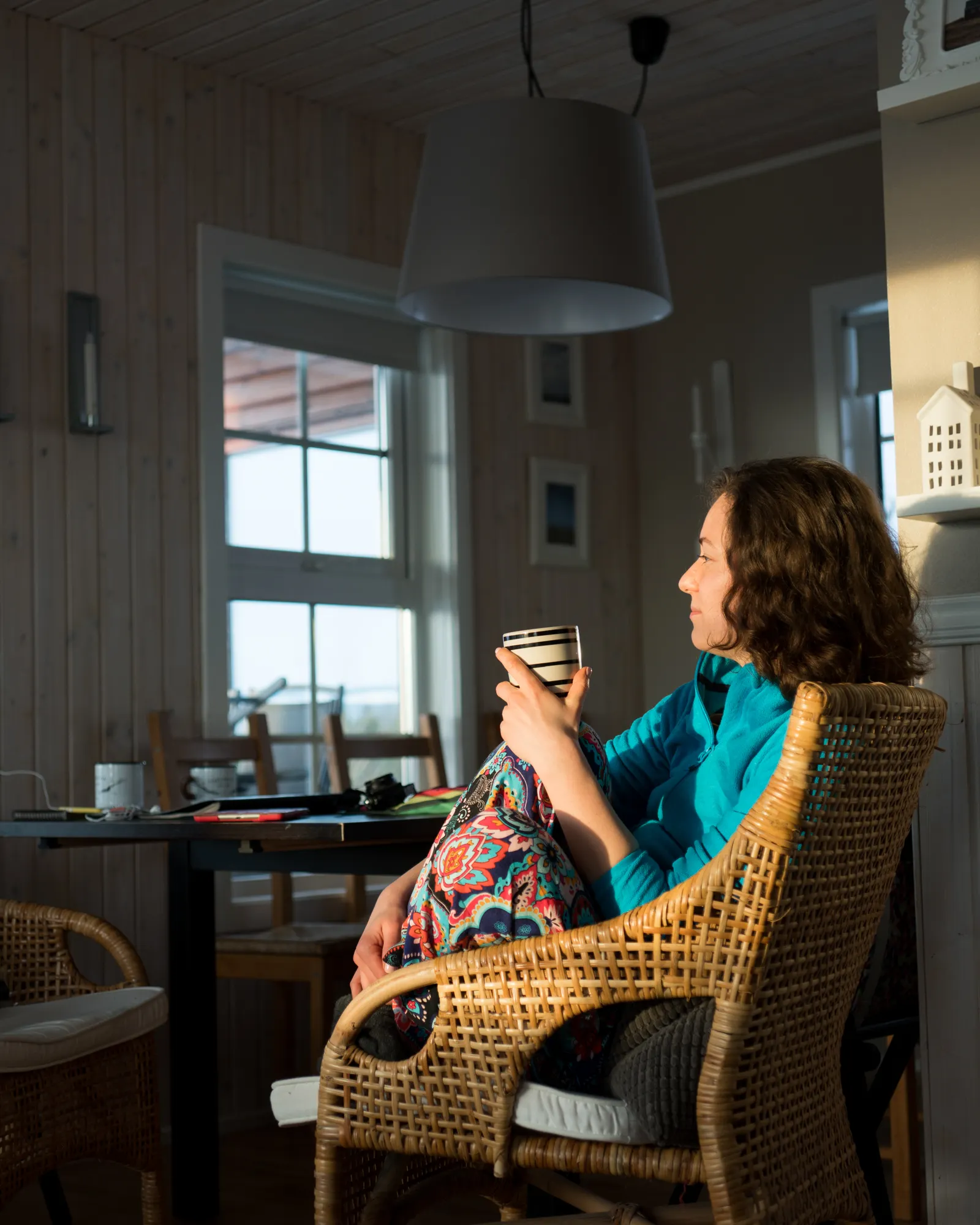 A woman sitting in a sunlit living room holding a warm mug, quiet and at ease.