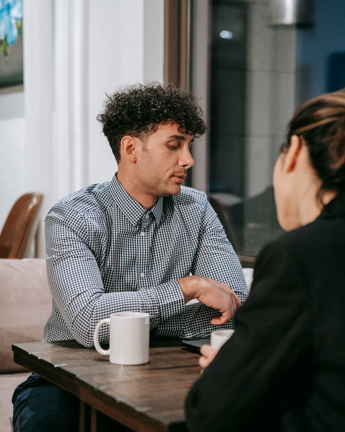A man and a woman sit across a table from each other, talking over coffee.