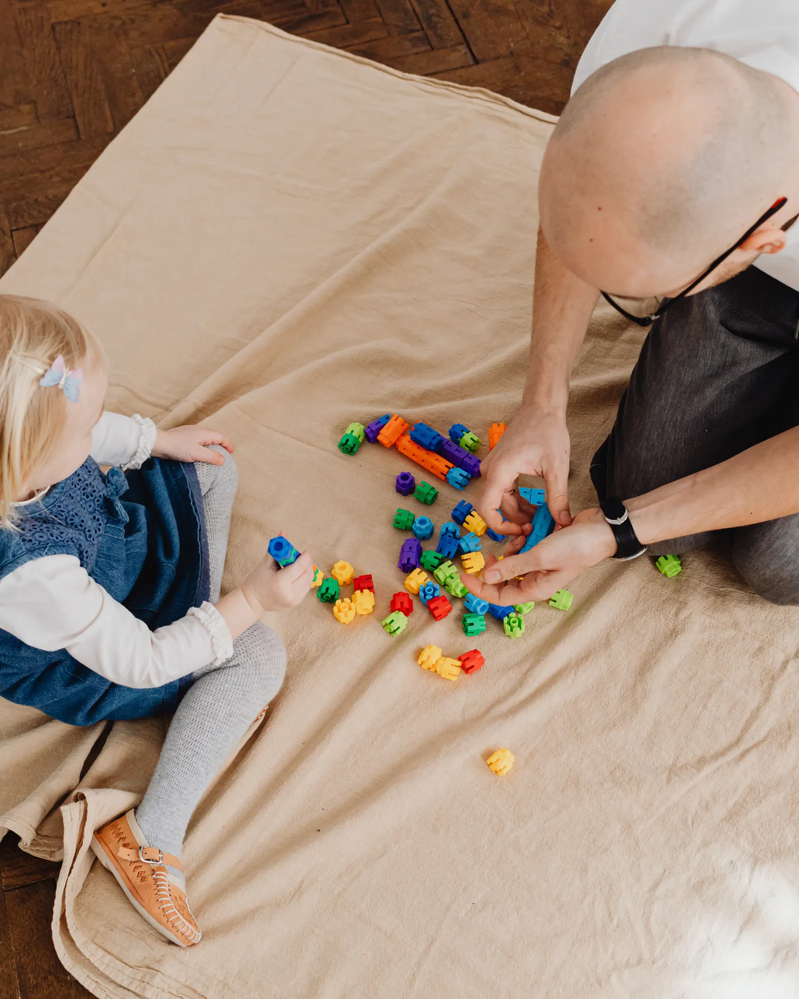 A father and his toddler daughter sit on the floor playing with colorful toys together.