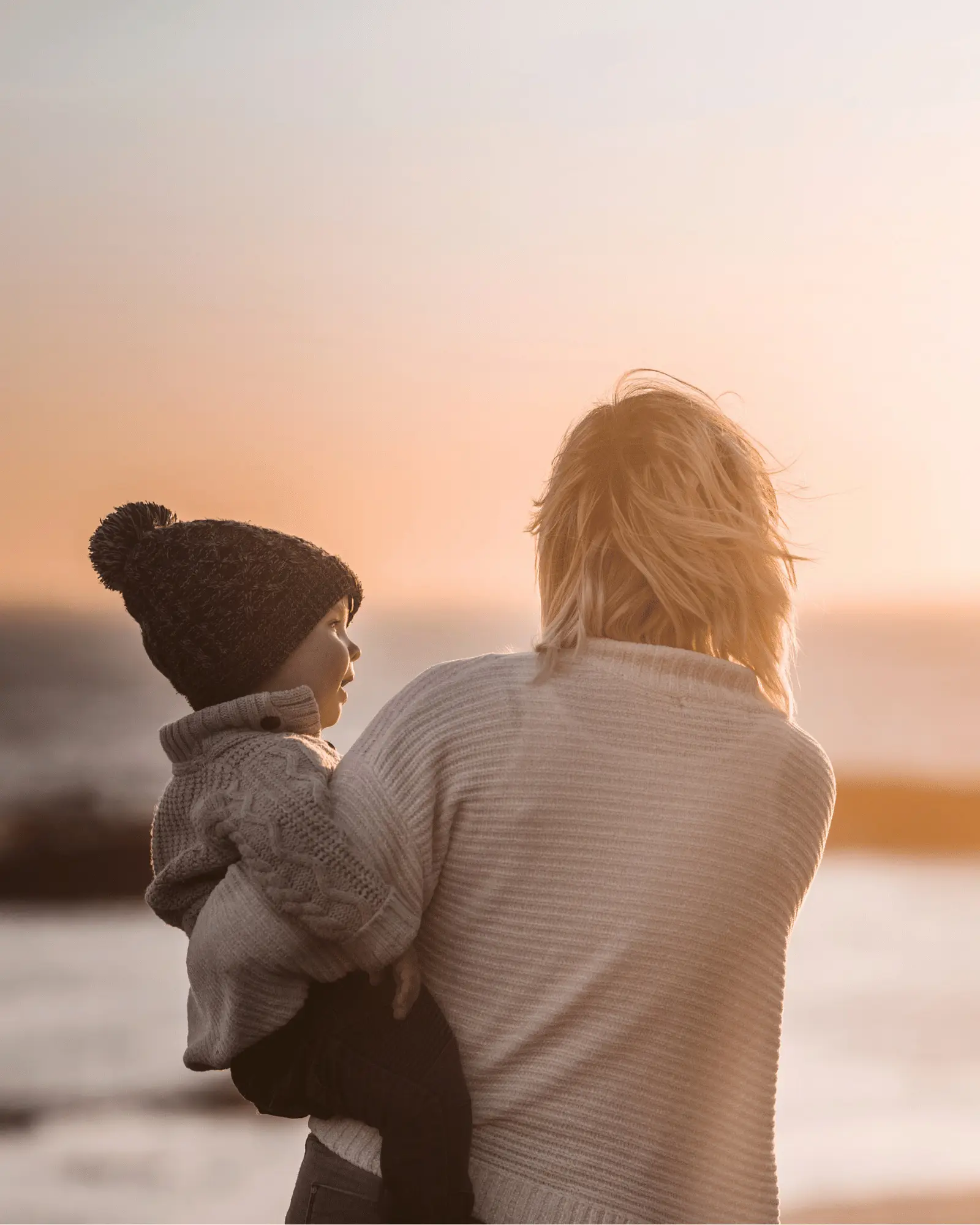 Adult holding a child while looking toward a seascape at sunset, conveying warmth and reassurance